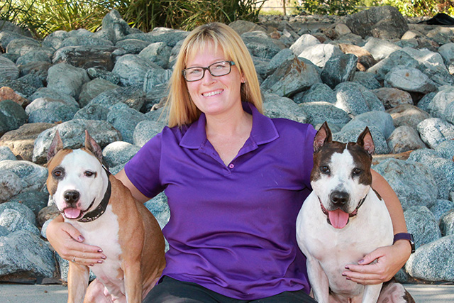A woman sits with two dogs next to her