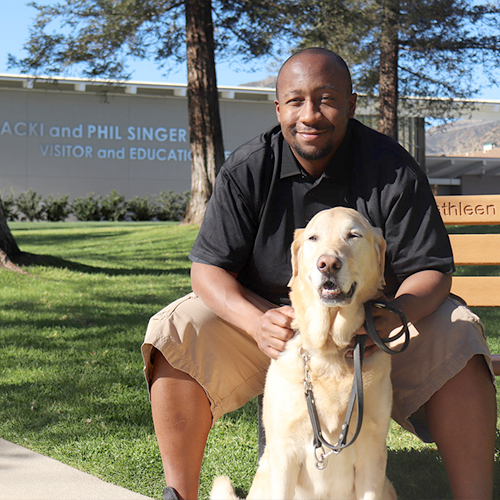 Headshot of Scott West sitting outside on a bench with a Yellow Lab dog.