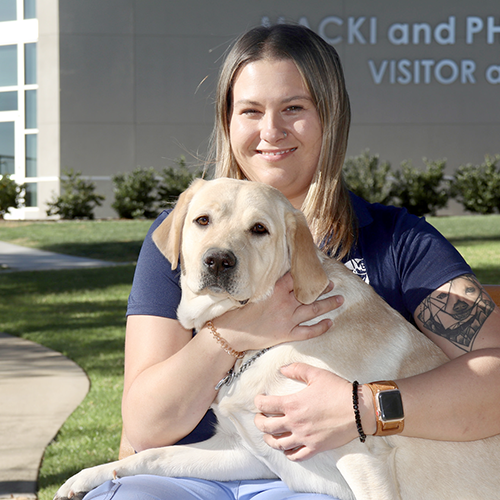 Headshot of Tiffanie Tayrien sitting outside with a Yellow Lab dog.