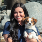 Headshot of Mariah Romo sitting outside and holding a dog.