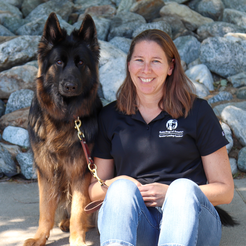 Headshot of Cheryl Herman sitting outside on rocks with a German Sheperd dog.