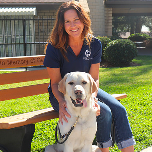 Headshot of Debra Grossman sitting on a bench with a Yellow Lab dog.