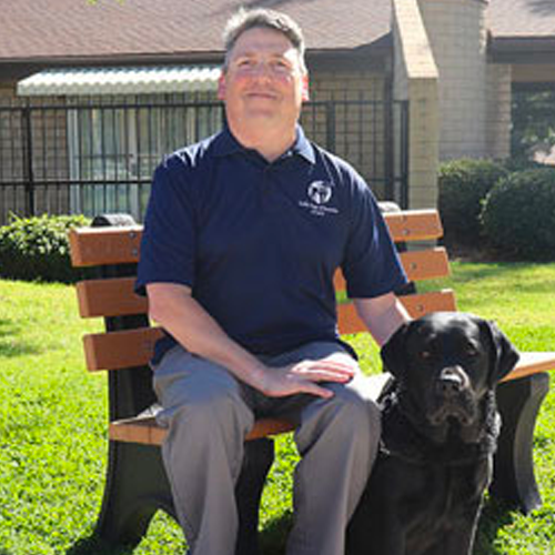 Headshot of Greg Steinmetz sitting on a bench with a Black Lab dog.