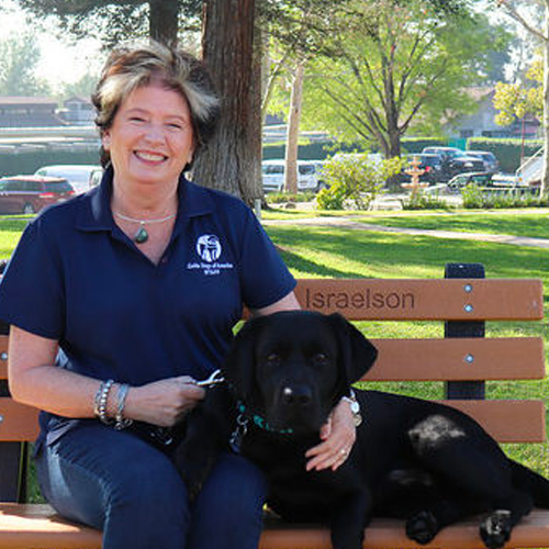 Headshot of Judy Reilly sitting on a bench with a Black Lab dog.