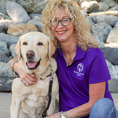 Headshot of Lorri Bernson sitting outside with her arm around a Yellow Lab dog.