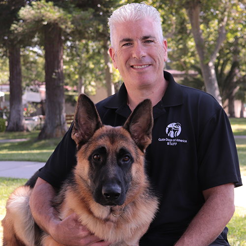 Headshot of Russell Gittlen sitting with his arm around a German Shepherd dog.