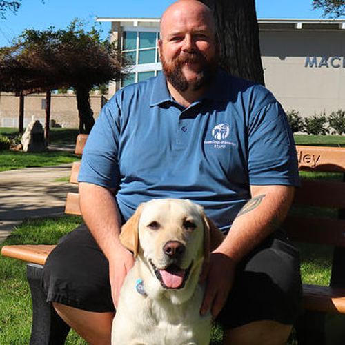 Headshot of Sean Chiles sitting outside with a Yellow lab dog.