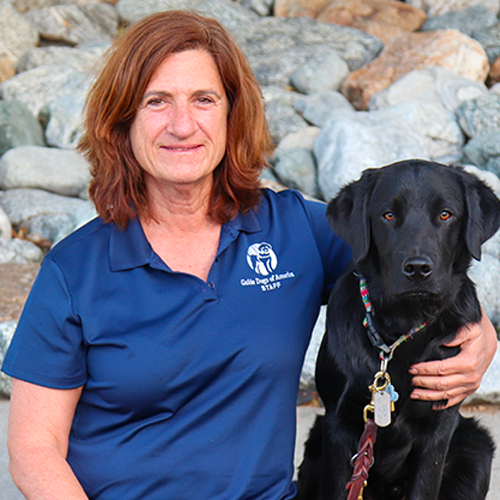 Headshot of Tracy Sampson sitting outside with their arm around a Black Lab puppy.