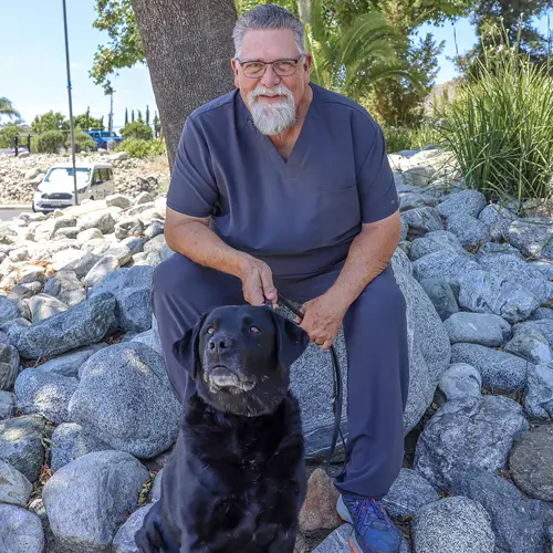 Headshot of Sandy Ralph sitting outside with his Black Lab dog.