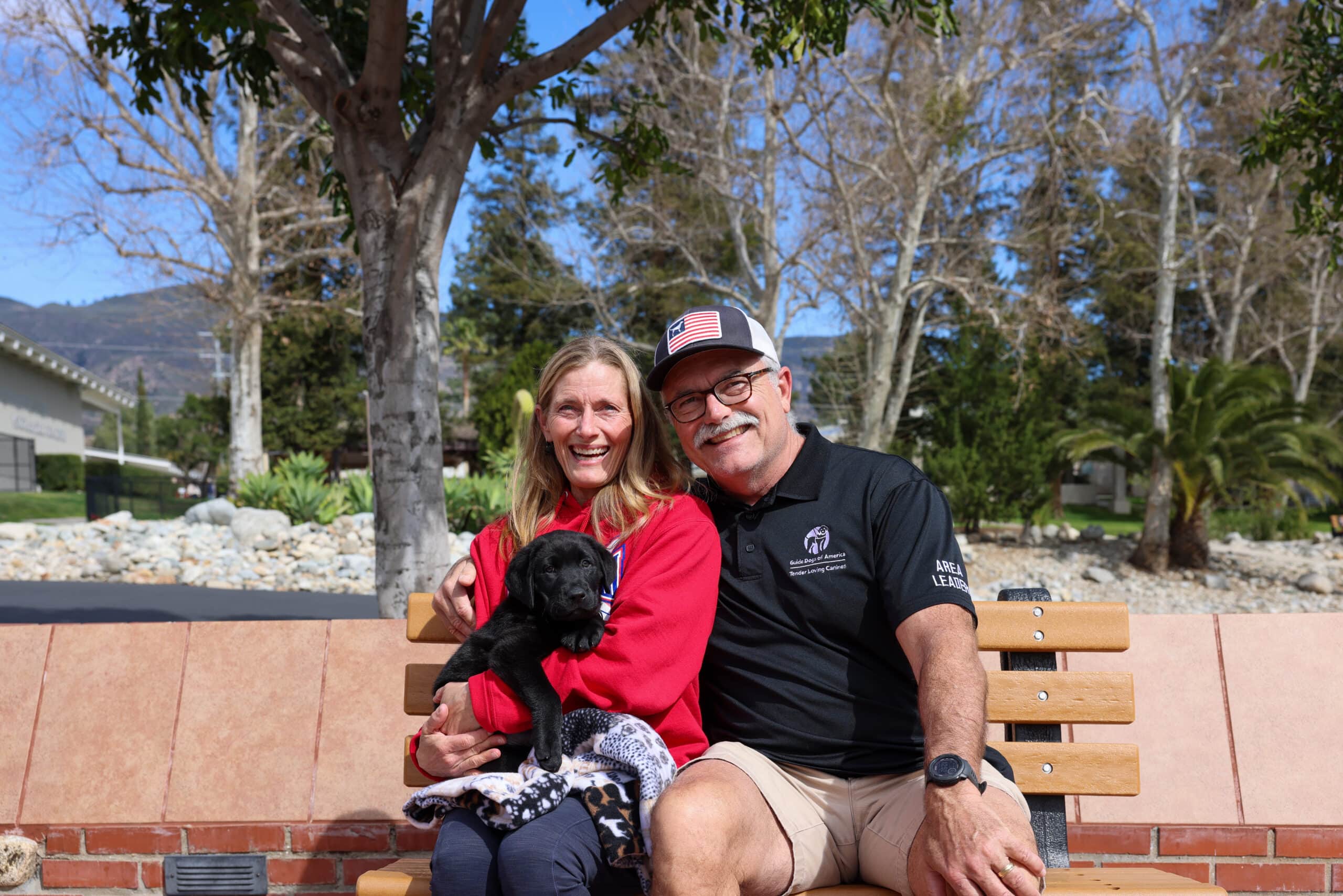 A man and a woman sitting on a bench with a dog in the womans lap.